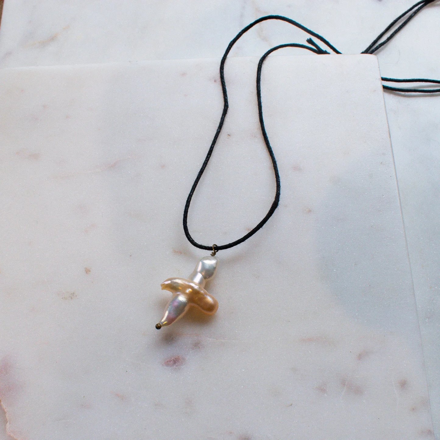 The NOIRÉE Pearl Cross Necklace on Black Cord